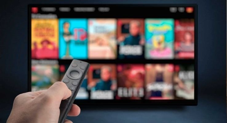 Pessoa usando controle remoto inteligente para navegar na interface da TV 3.0 com recursos de streaming e interatividade.